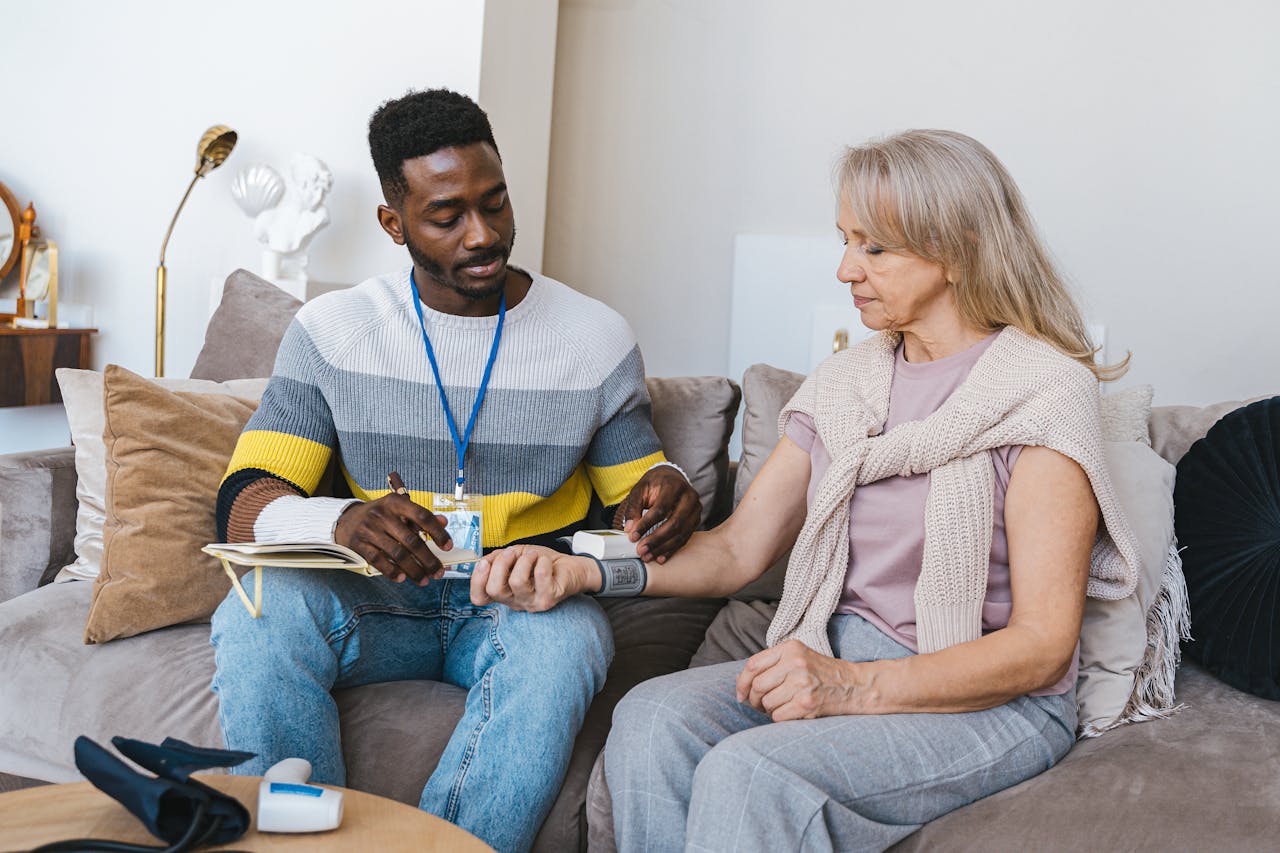 Home Volunteer checking elderly woman's blood pressure at home. Compassionate healthcare support.
